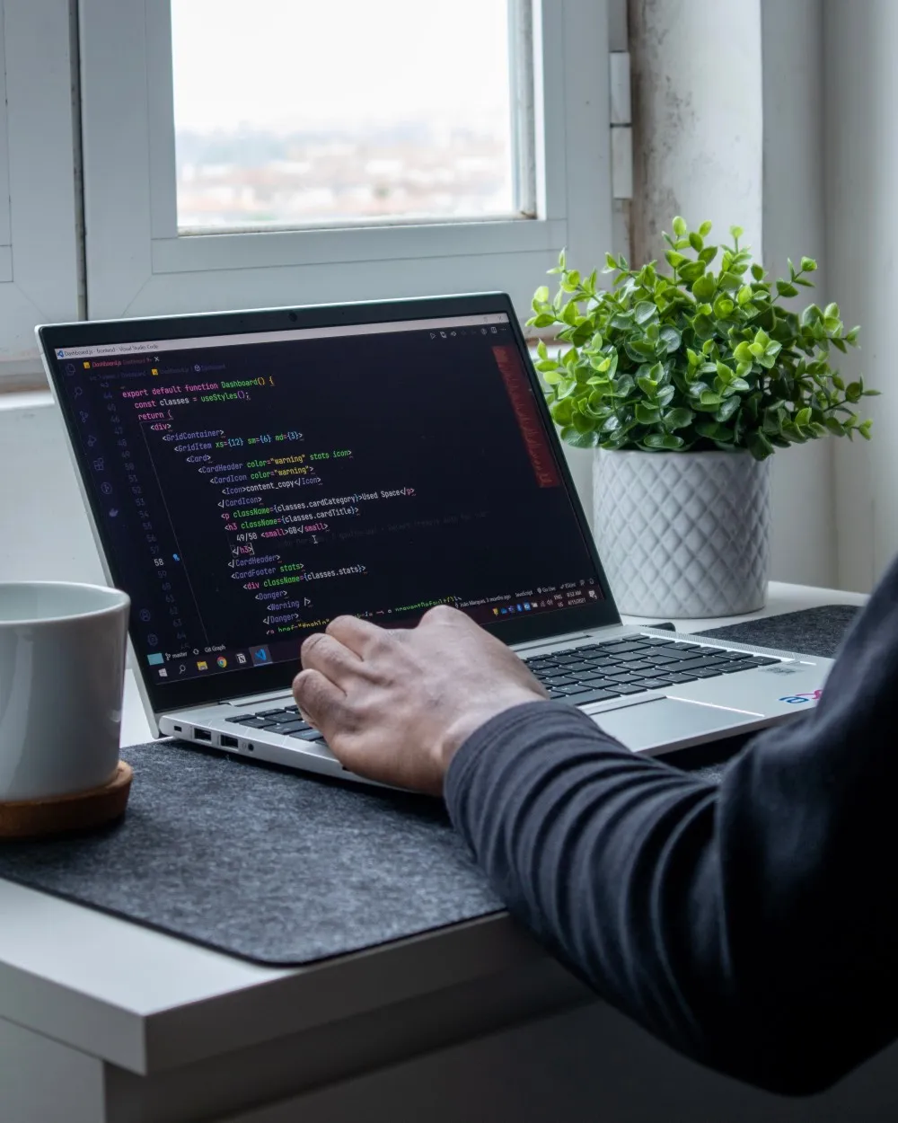 Person typing code on a laptop by a window